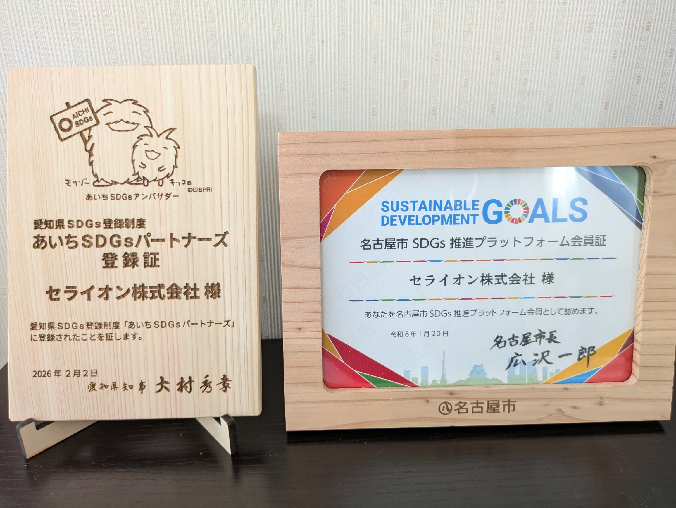 セライオン株式会社が受領した、あいちSDGsパートナーズ登録証(木製・モリゾーとキッコロ刻印)と名古屋市SDGs推進プラットフォーム会員証(厚さ2cmの木製スタンド付き)が並んだ写真。愛知県と名古屋市の両自治体からSDGs推進企業として認定